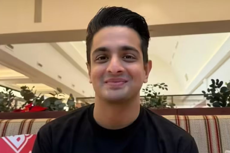 Raveer Allahbadia smiling indoors while sitting at a café-style setting with plants in the background