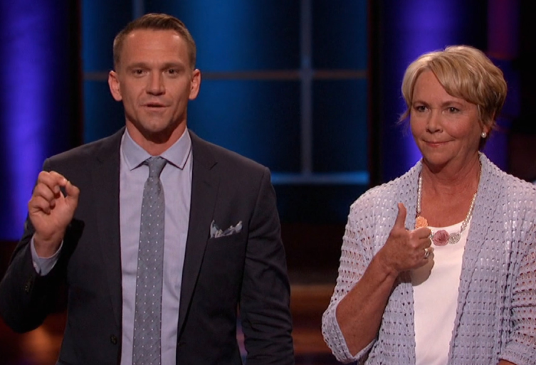 Bobby Edwards and Judy Edwards, the founders of Squatty Potty, appearing on the set of Shark Tank US. Bobby is wearing a suit and gesturing while speaking, and Judy is standing beside him in a blue cardigan giving a thumbs-up against the show's signature blue-lit background.